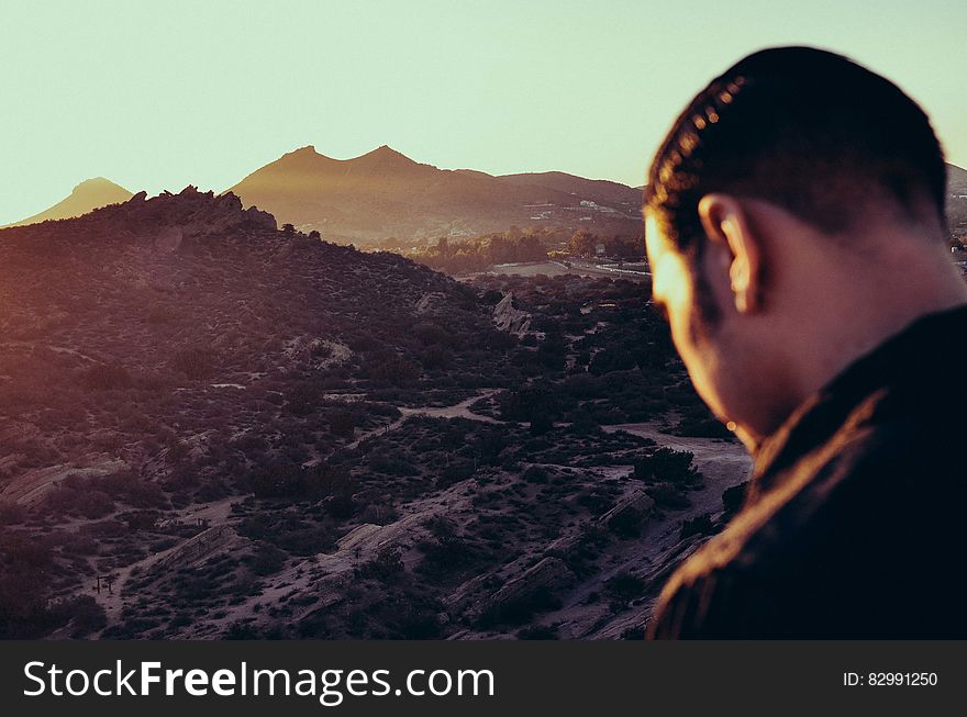 Back of man overlooking mountain valley on sunny day.