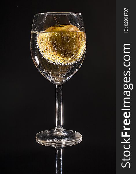 Clear Wine Glass Filled With Clear Beverage With Yellow Round Fruit