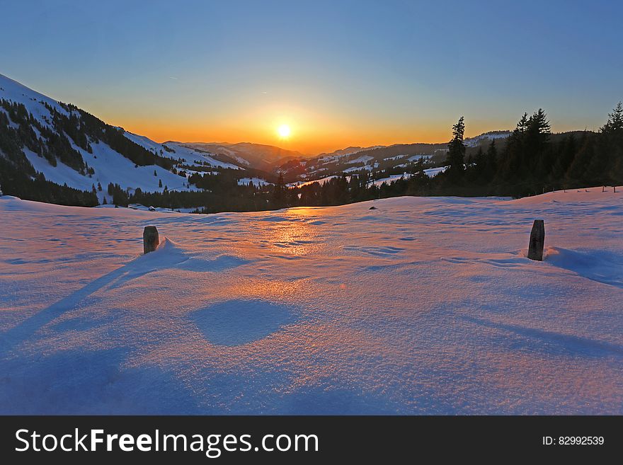 Sun Rising In Horizon Over Snow Coated Mountains