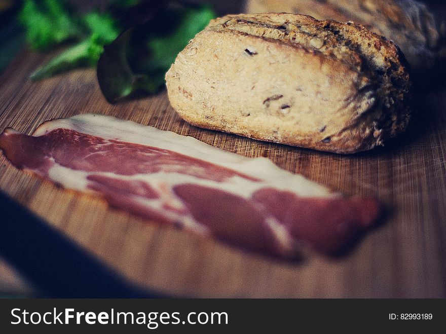 Close up of sliced bacon and bread with lettuce on wooden cutting board.