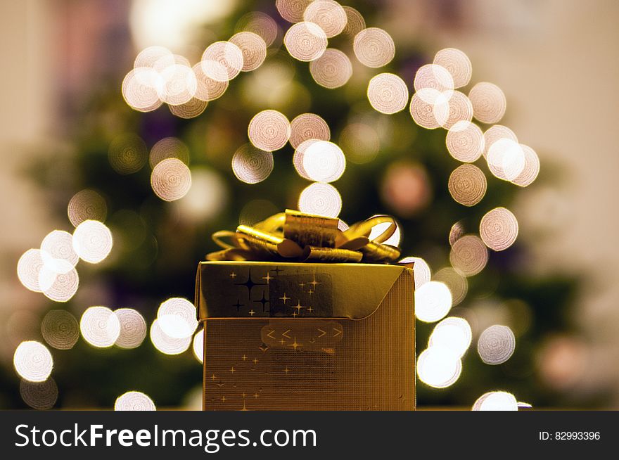 Golden gift in front of bokeh lights on Christmas tree.