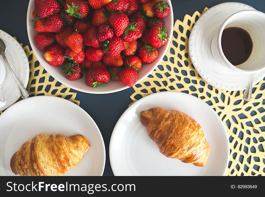 Fresh buttery croissants, hot cup of coffee and bowl with strawberries