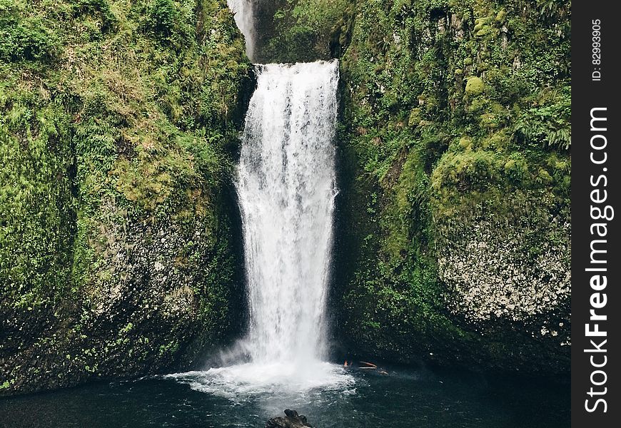 Waterfall over green cliff into countryside pool. Waterfall over green cliff into countryside pool.