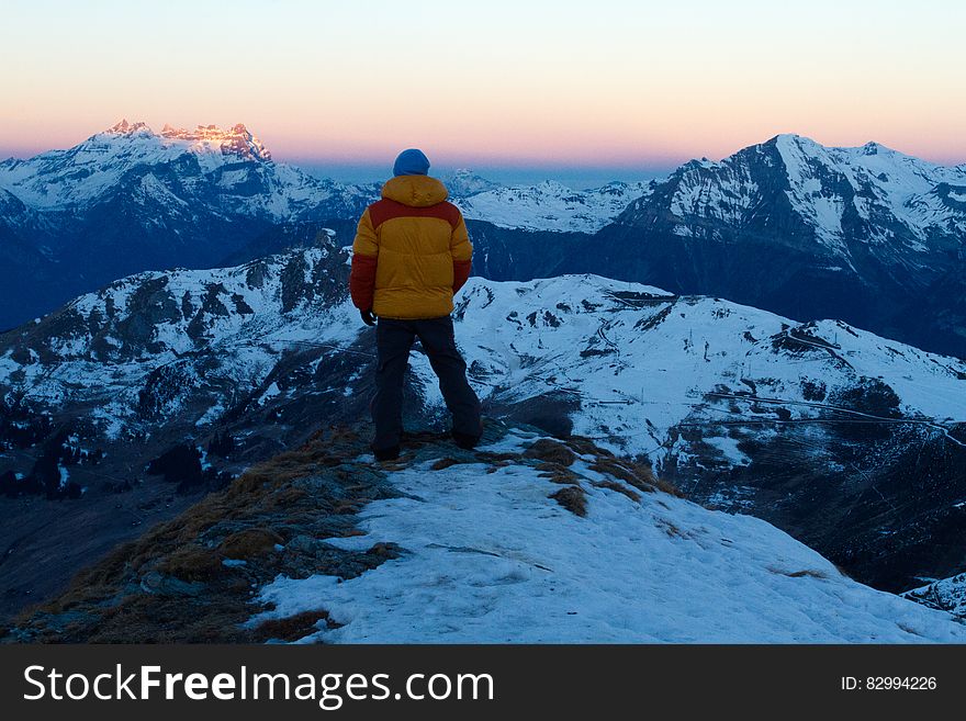 Person in Orange and Red Winter Jacket on Top of Snow Covered Mountain