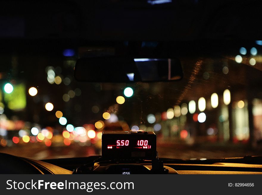 View through windscreen of taxi cab driving through city at night with fare meter in foreground. View through windscreen of taxi cab driving through city at night with fare meter in foreground.