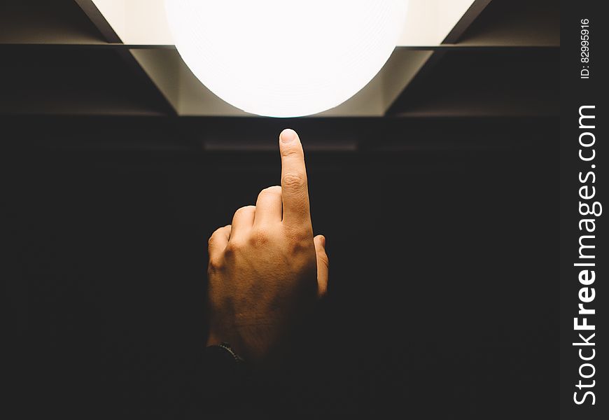 Close up of finger reaching from darkness touching white lamp. Close up of finger reaching from darkness touching white lamp.