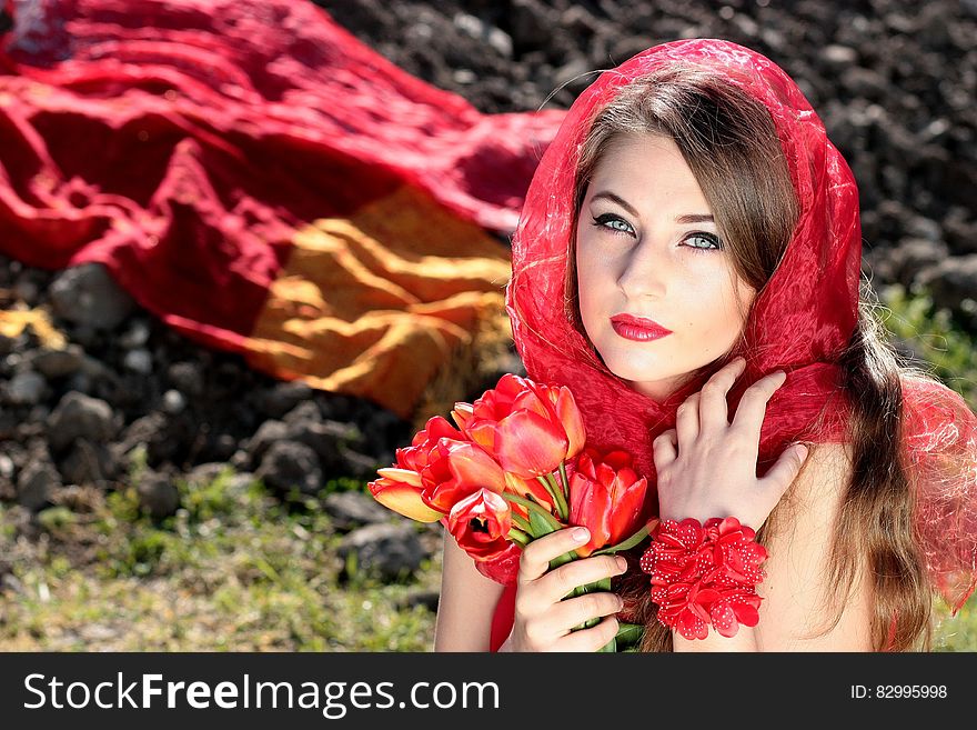 Woman Wearing a Red Scarf Holding Red Flowers