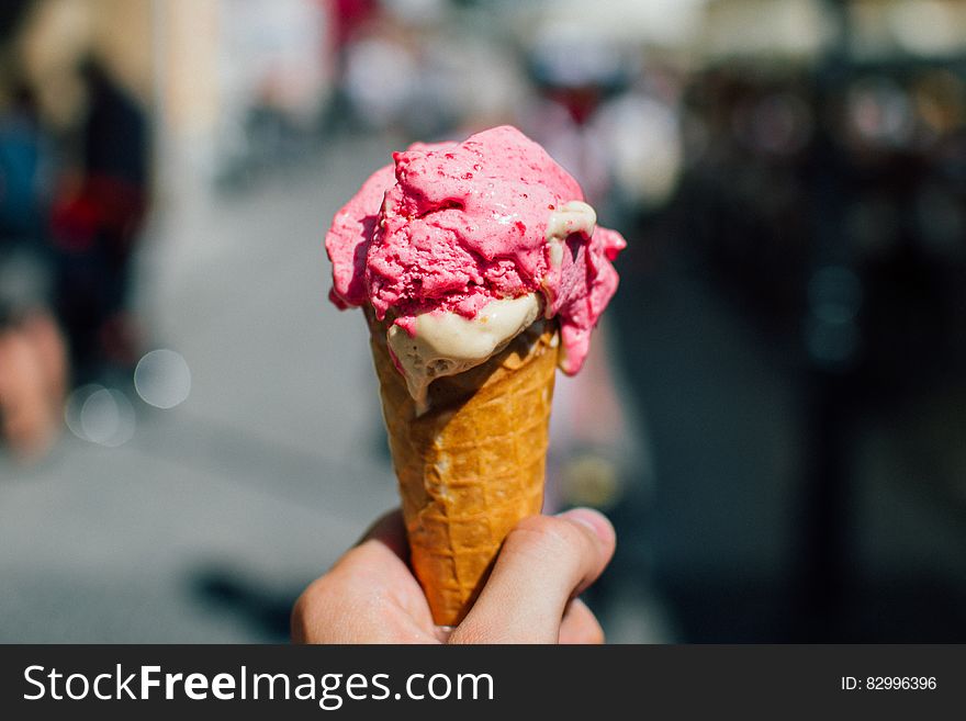 Hand of person holding strawberry ice cream cone outdoors. Hand of person holding strawberry ice cream cone outdoors.