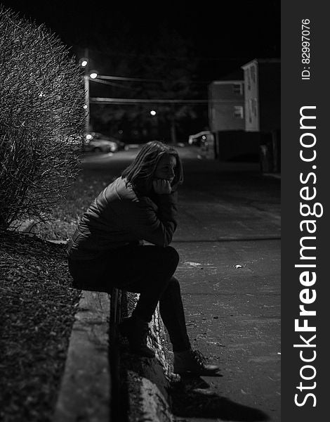 Woman Wearing Jacket Sitting on Concrete during Night Time