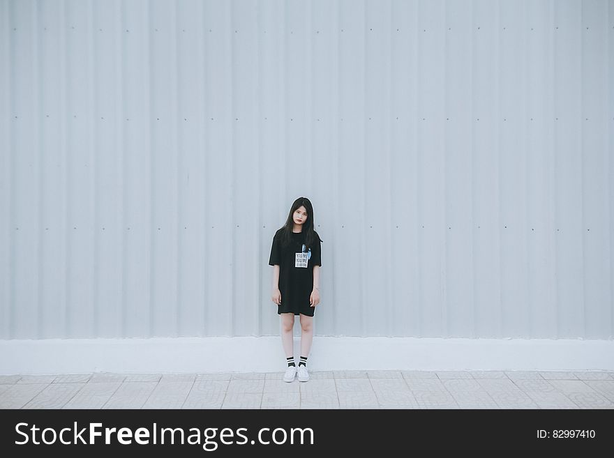 Woman In Black Elbow Sleeve Shirt And Black Shorts Standing Behind White Wall