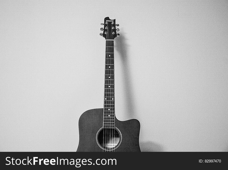 Close up of acoustic guitar against wall in black and white.