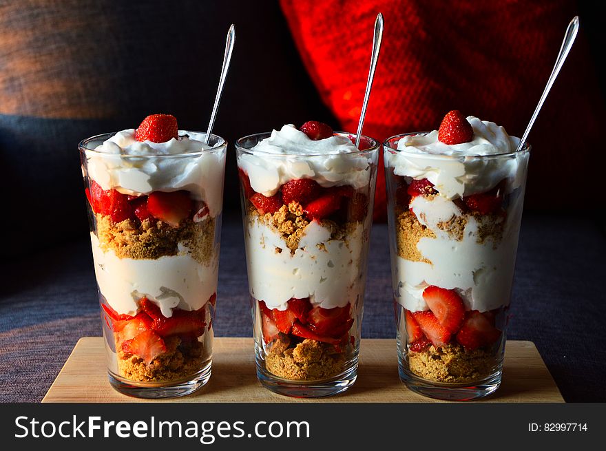 Strawberry and granola parfait sundaes on wooden tray.