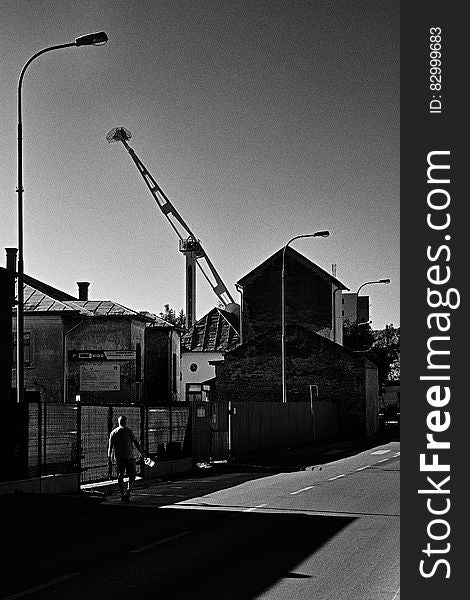 Man walking along fence line of industrial lot in urban black and white scene. Man walking along fence line of industrial lot in urban black and white scene.