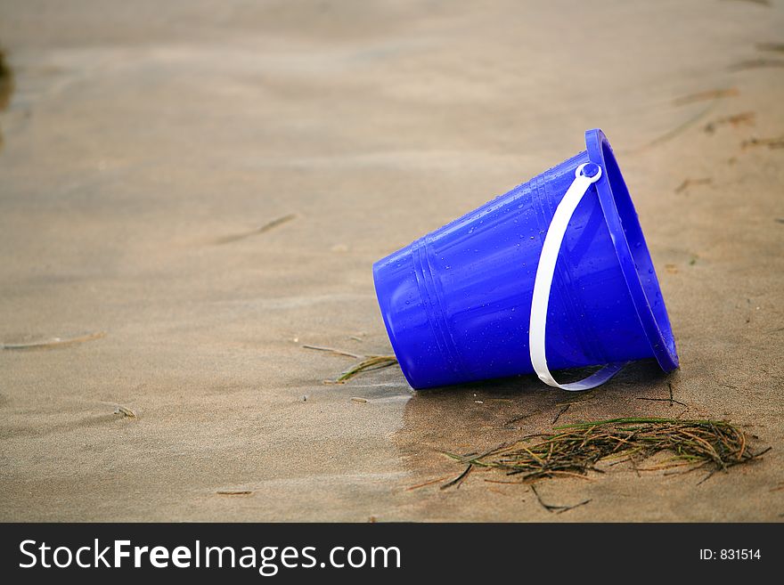 Close up image of a wet sand blue bucket alone in the tropical sand. Close up image of a wet sand blue bucket alone in the tropical sand