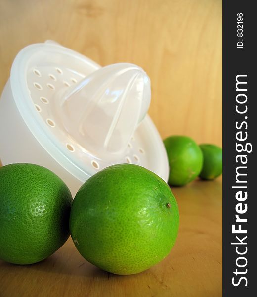A fruit squeezer with fresh green limes. Focused at the limes in the foreground. A fruit squeezer with fresh green limes. Focused at the limes in the foreground.