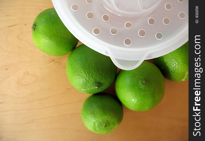 A fruit squeezer with fresh green limes. Focused at the fruit squeezer. A fruit squeezer with fresh green limes. Focused at the fruit squeezer.