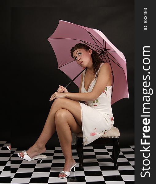 Beautiful young woman in white dress sitting under pink umbrella and checking to see if it is raining