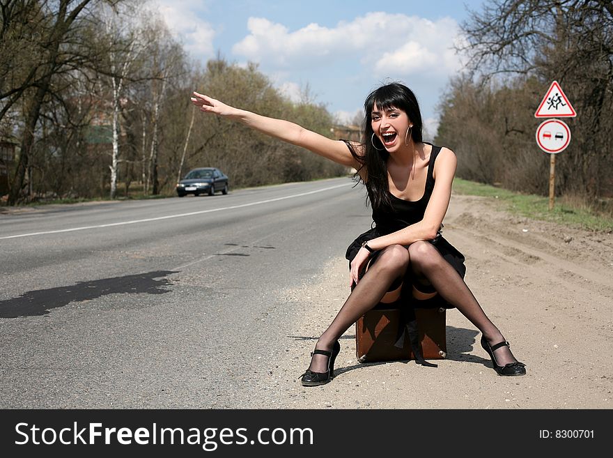 Lovely girl in the road sit atop vintage suitcase