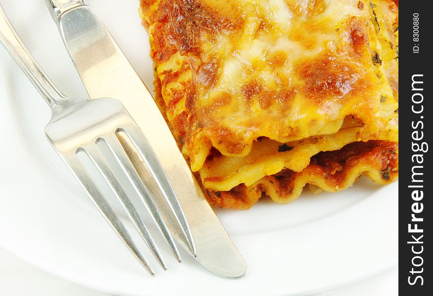 Serving of spinach lasagna close up with a knife and fork on a white plate. Serving of spinach lasagna close up with a knife and fork on a white plate.