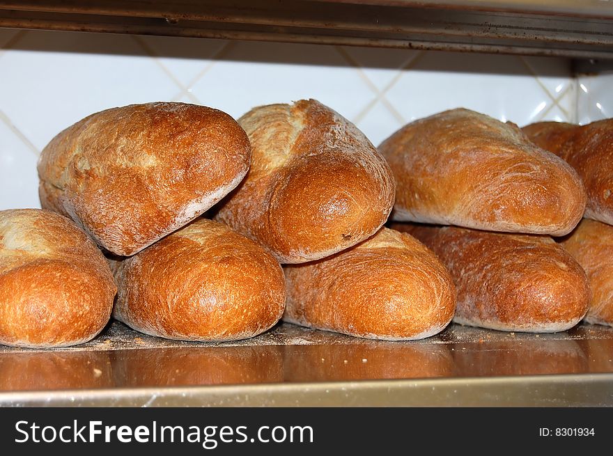 This is a shot of some bread loaves on a stainless steel shelf ready to be cut and served.