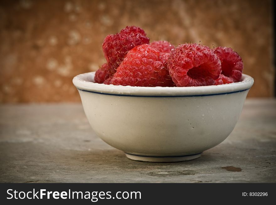 Ripe raspberries in small bowl on slate background.