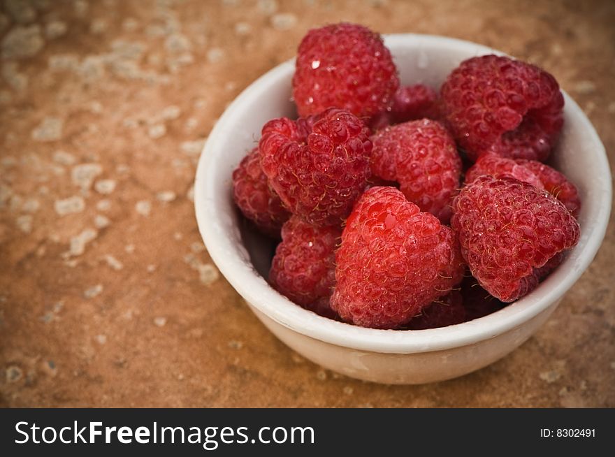 Ripe raspberries in small porcelain bowl on pink slate. Ripe raspberries in small porcelain bowl on pink slate.