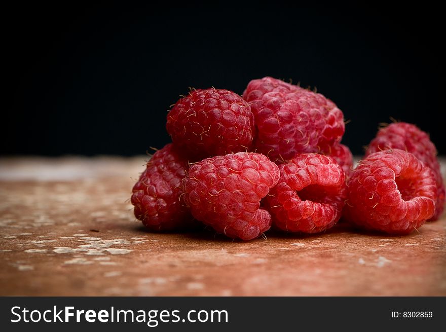 Several ripe raspberries on pink slate and black background.