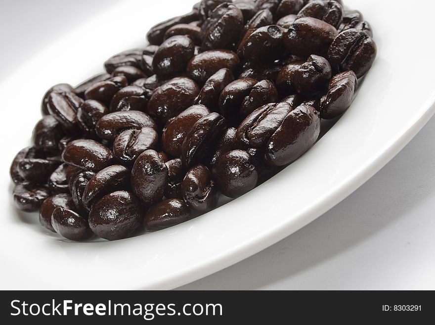 A white plate with coffee beans. Light from above left; reflection in beans.