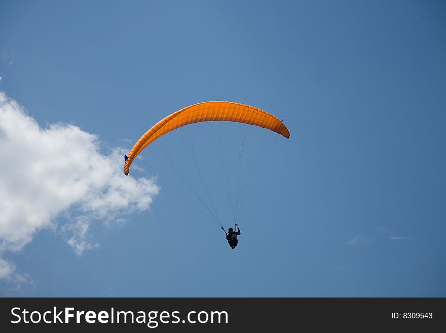A Paraglider flies in the blue sky.
