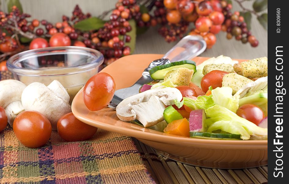 Colorful garden salad with mushrooms, tomatoes, and Italian dressing in orange bowl with fall colored table setting copy space