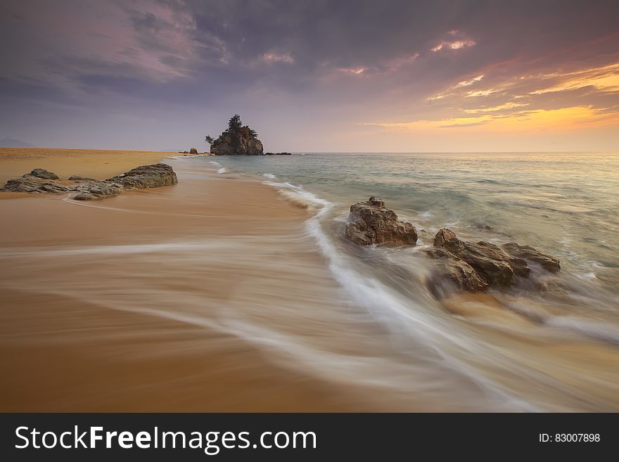 Waves over sandy beach on Bora Bora at sunset.