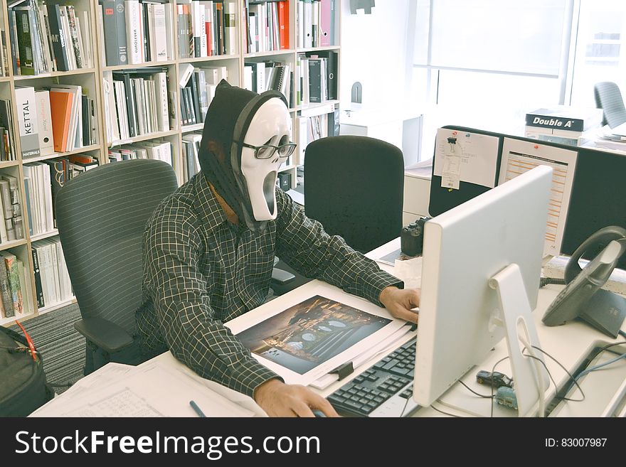 Person Wearing Scream Mask and Black Dress Shirt While Facing Computer Table during Daytime