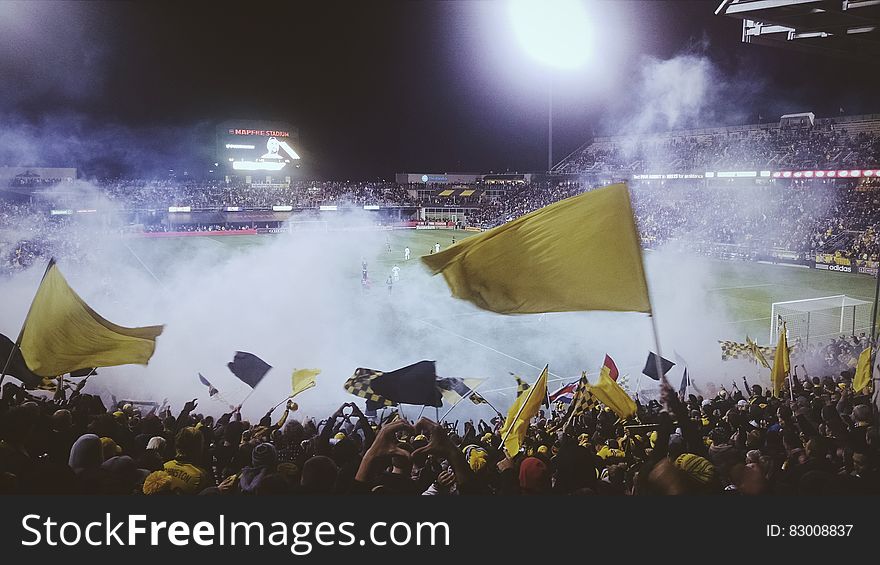 Big crowds attending a football match waving yellow flags but play not visible due to smoke from fireworks set off by hooligans. Big crowds attending a football match waving yellow flags but play not visible due to smoke from fireworks set off by hooligans.