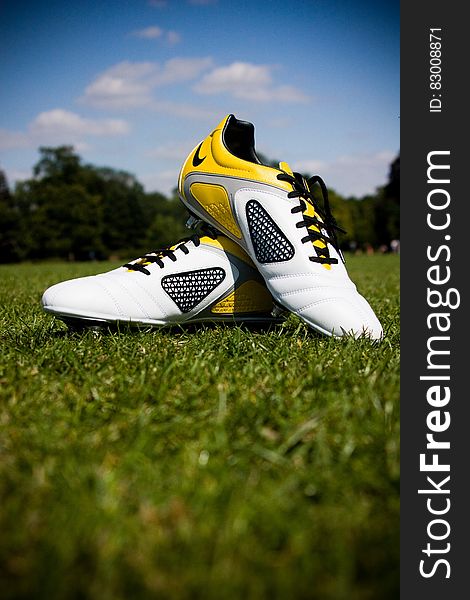 Closeup of designer sports shoes in yellow, black and white colors placed artistically on grass with selective focus.