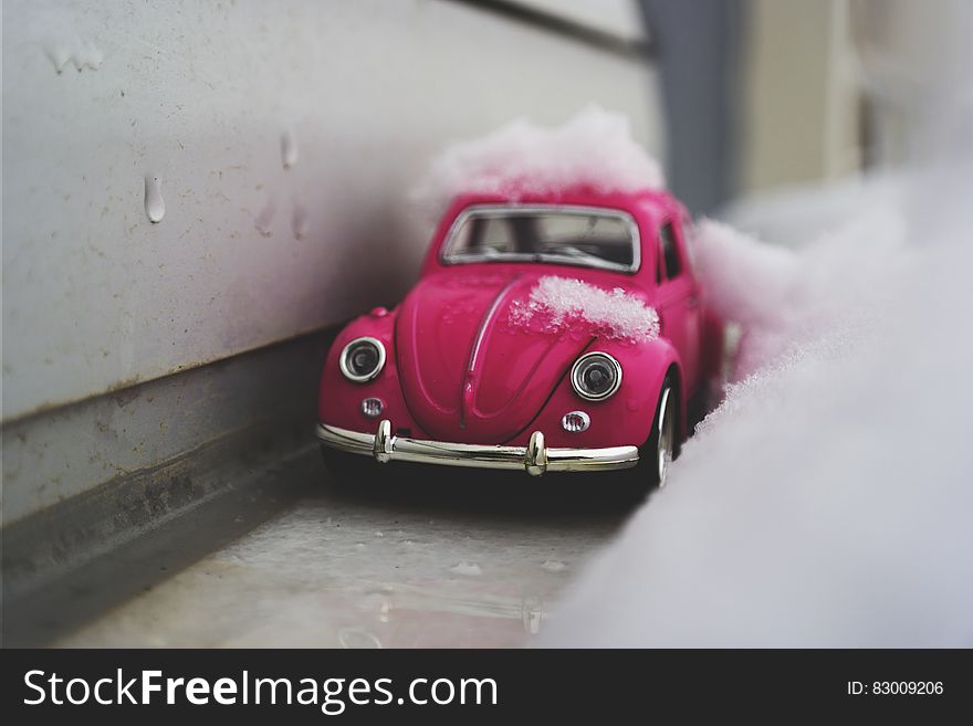 Close up of toy pink Beetle car covered in snow next to exterior wall. Close up of toy pink Beetle car covered in snow next to exterior wall.
