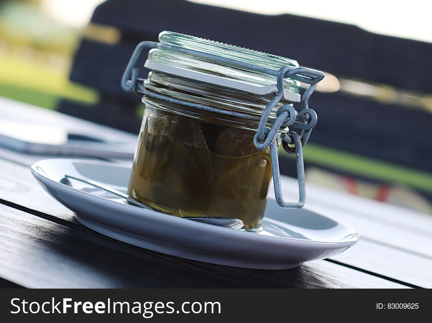 Jar of jalapeno preserves on white plate on wooden tabletop.