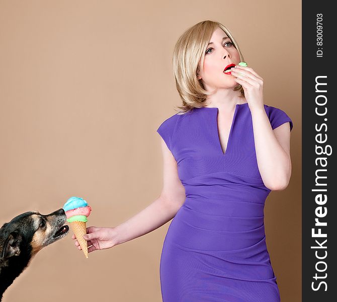 Woman in Purple Split Neck Cap Sleeve Bodycon Dress Holding Cone of Ice Cream Licked by Black Tan Dog