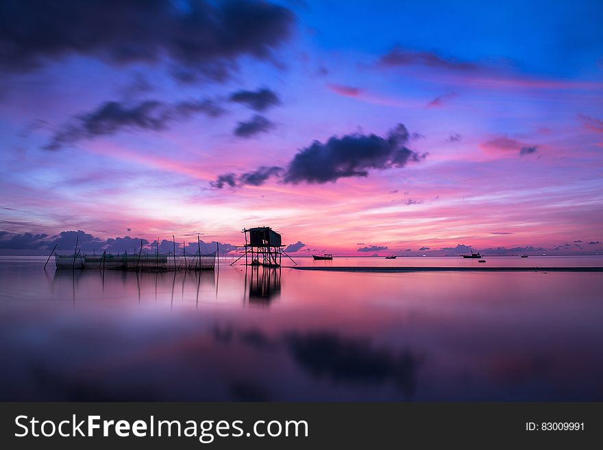 Scenic view of colorful sunset and cloudscape over tropical stilt houses on calm sea. Scenic view of colorful sunset and cloudscape over tropical stilt houses on calm sea.