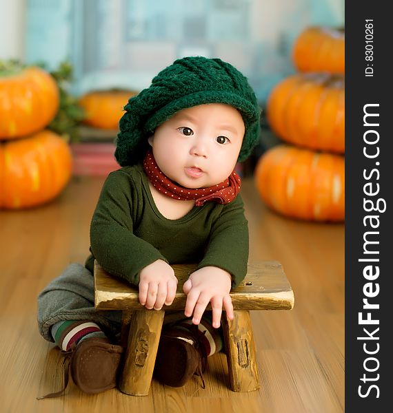 An Asian child leaning on a small stool with pumpkins on the background. An Asian child leaning on a small stool with pumpkins on the background.