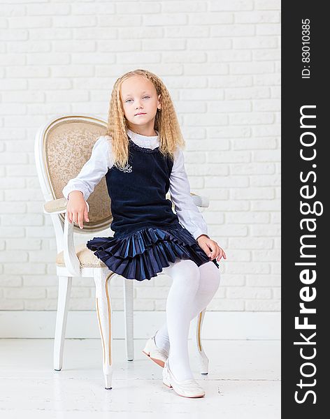 Portrait of young girl sitting in chair wearing blue dress and tights.