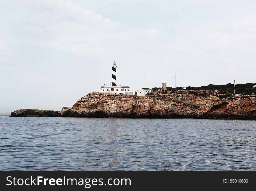 A lighthouse on a rocky cape and still sea surface around. A lighthouse on a rocky cape and still sea surface around.