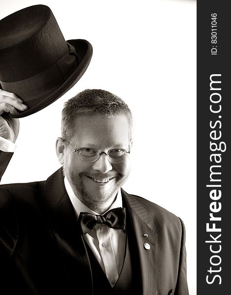 Man In Tuxedo And Eyeglasses Holding Top Hat In Grayscale