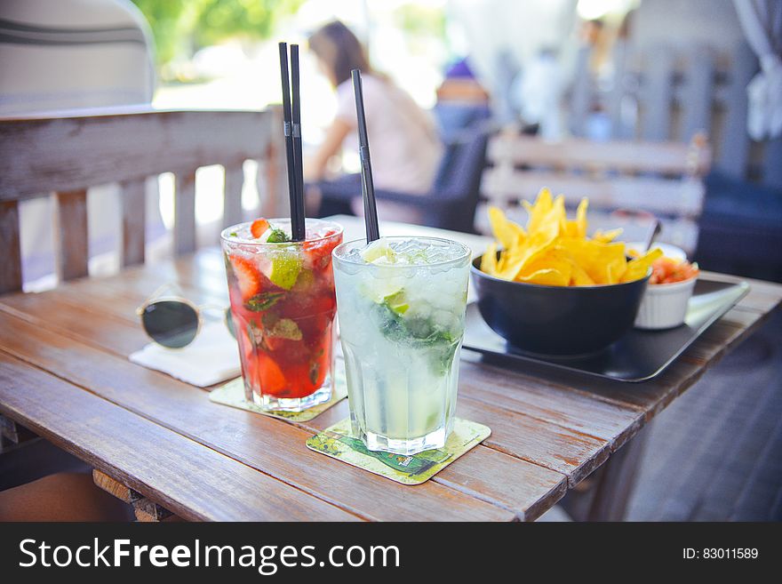 Close up of drinks and snacks on wooden outdoor table on sunny day. Close up of drinks and snacks on wooden outdoor table on sunny day.