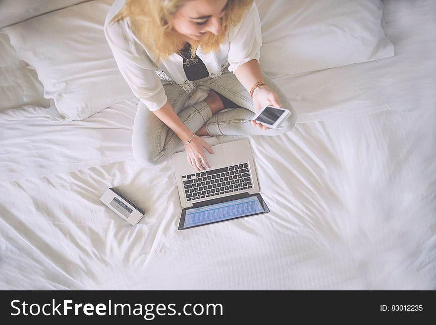 Elevated view of blond businesswoman on bed using Apple Macbook and Iphone.