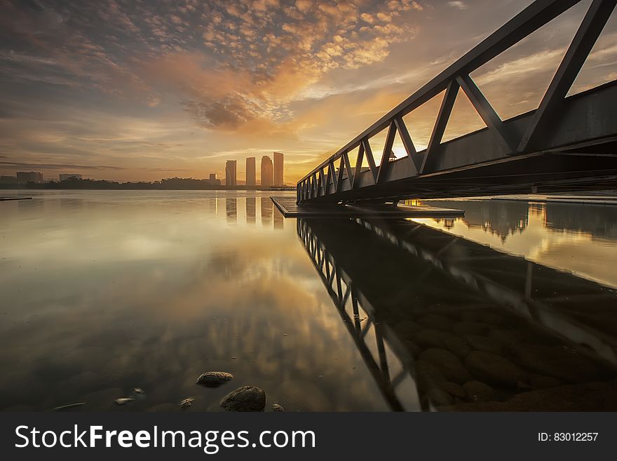 Bridge over sea with city skyline at sunset