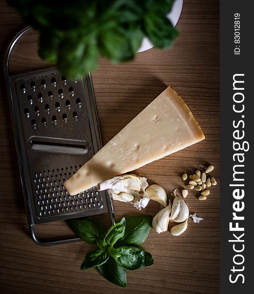 Ingredients for pesto including Parmesan cheese wedge and grater, garlic, pine nuts and fresh basil on wood. Ingredients for pesto including Parmesan cheese wedge and grater, garlic, pine nuts and fresh basil on wood.