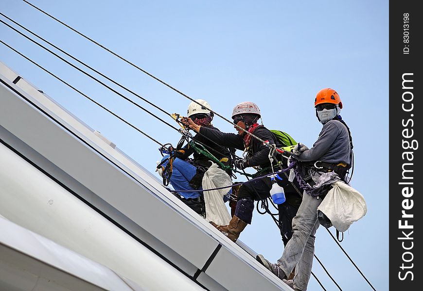 A group of workers hanging on the side of a building on safety harnesses and ropes. A group of workers hanging on the side of a building on safety harnesses and ropes.