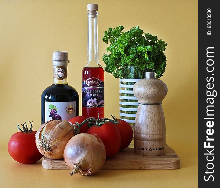 Fresh tomatoes, onions and herbs on cutting board with vinegar and condiments, studio background. Fresh tomatoes, onions and herbs on cutting board with vinegar and condiments, studio background.