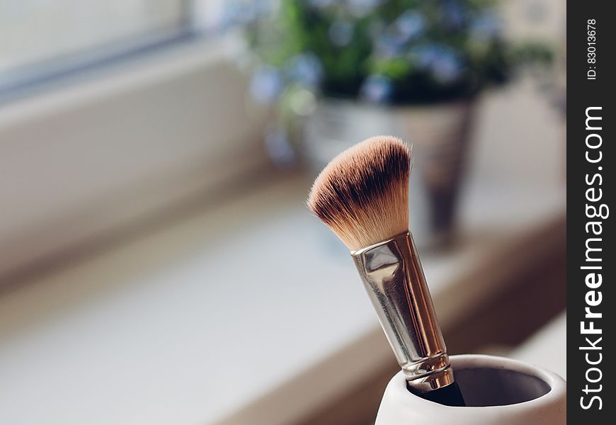 Make-up brush in cup next to sunny window.