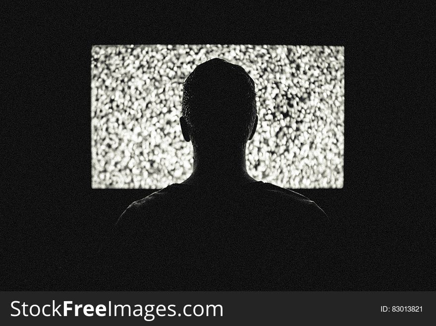 Silhouette of young man watching screen (cinema or television or computer) with noise on it; concept of wasting time instead of doing something useful. Silhouette of young man watching screen (cinema or television or computer) with noise on it; concept of wasting time instead of doing something useful.
